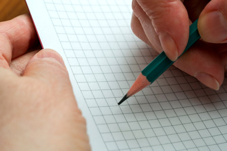 A person is carefully drawing on grid paper with a colored pencil, showing creativity.の写真素材