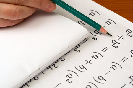 A hand grips a pencil, solving algebraic equations in a cozy study environment.の写真素材