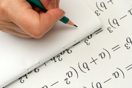 A hand grips a pencil, focused on solving complex equations in a notebook.の写真素材