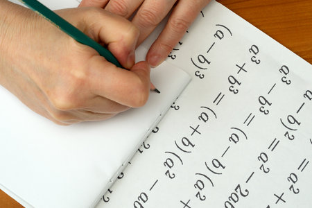 Hands carefully solve mathematical equations on a notepad at a wooden desk.の写真素材