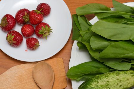 Bright red strawberries and fresh green spinach await preparation on a wooden surface.の写真素材