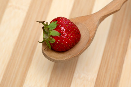 A vibrant strawberry balanced on a handcrafted wooden spoon in a cozy kitchen.の写真素材