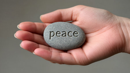 A hand supports a smooth stone engraved with the word peace, symbolizing tranquility.の素材