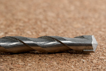 Close-up view of a metallic drill bit placed on a textured surface, showing intricate details.