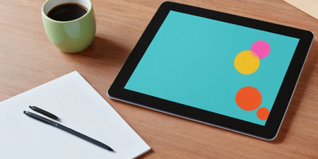 A vibrant tablet displays colorful shapes beside a cup of coffee and stationery.の素材