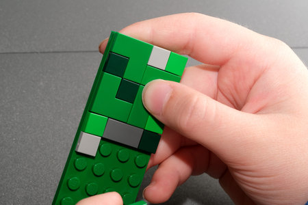 A hand skillfully assembles vibrant green building blocks into a unique creation.