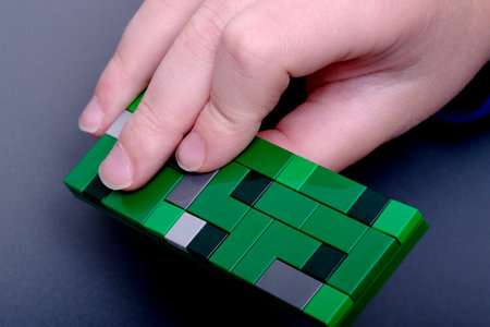 A child's hand presses down on a green block structure, showing creativity.の写真素材