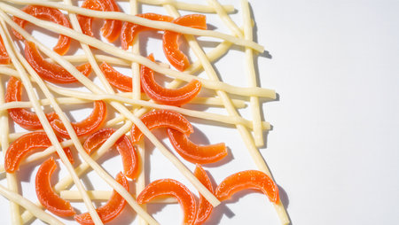 Bright orange candy pieces and thin white sticks lay scattered artistically.の素材