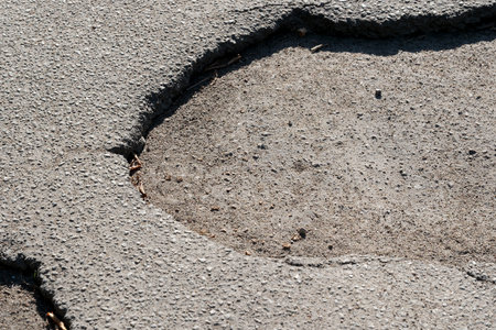 A large pothole disrupts the smooth asphalt surface under bright sunshine.