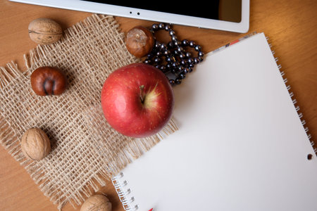 A bright red apple and nuts sit beside a blank notebook on a wooden surface.