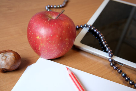 A shiny red apple sits next to a tablet and blank paper, creating warmth.