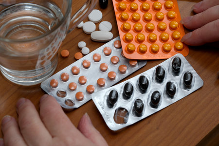 Hands sorting through different medicines alongside a glass of water.