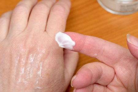 A hand gently spreads cream on fingers in a warm, inviting space.の写真素材