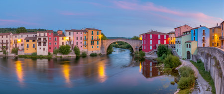 Colorful buildings line the riverbank while the sun sets, casting warm reflections.の素材