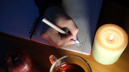 A person writes notes by candlelight, sipping tea and with an apple nearby.の写真素材