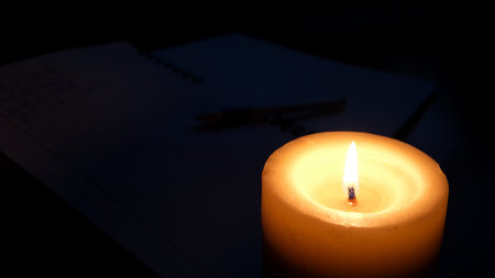 A warm candle glows softly beside a notebook in low light, inviting thoughts and peace.の写真素材