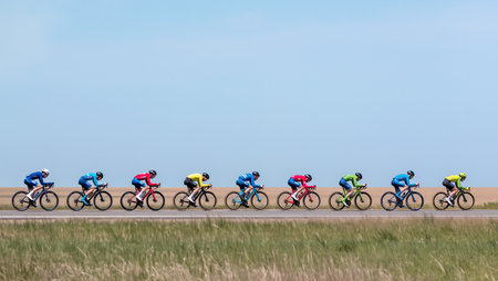 A group of cyclists competes on a wide road surrounded by grasslands in bright daylight.の素材