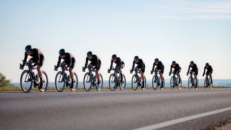 A group of cyclists rides closely together, speeding along an open road under a clear sky.の素材