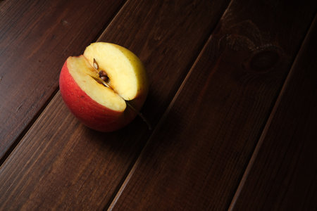 Bright red and yellow apple, freshly cut, lies on a rustic wooden table.の写真素材
