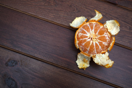 Bright tangerine sits on rustic wooden surface, its peel shaped like a turtle shell.の写真素材