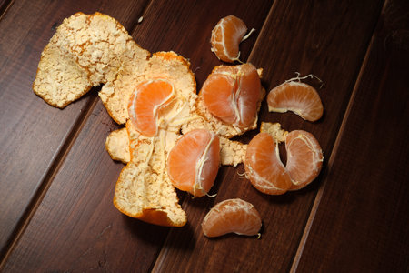 Juicy orange segments and vibrant peels are arranged on a rich wooden table.の写真素材