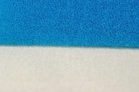 A bright blue sponge lies on a clean, soft white backdrop, inviting touch and use.の写真素材