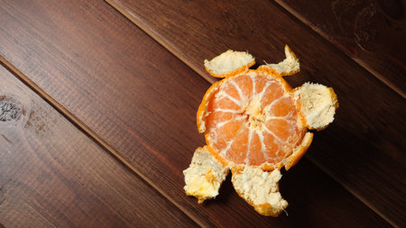 A playful turtle shape crafted from an orange peel rests on a wooden table.の写真素材