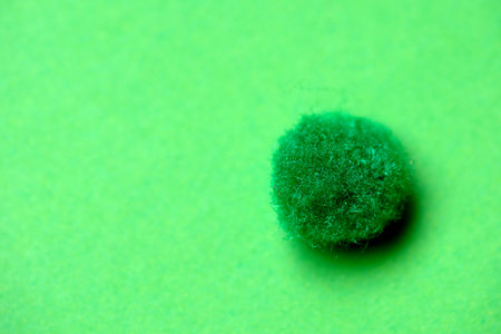 Tiny textured ball glows softly against a bright green backdrop in warm light.