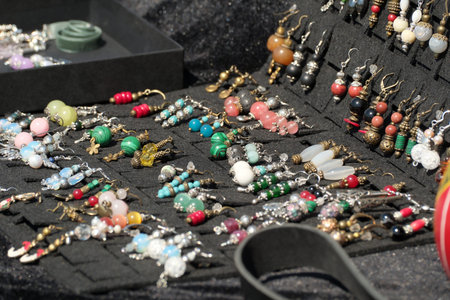 Intricate earrings sparkle under the sun at an outdoor artisan market filled with life.