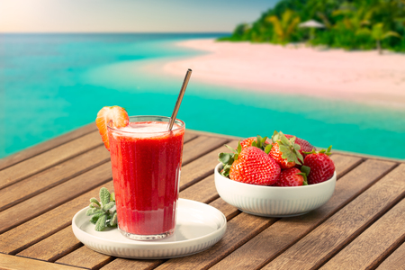 Vacation scene with fresh strawberry smoothie and tropical beach at background on sunny day. Vacation or leisure conceptの写真素材