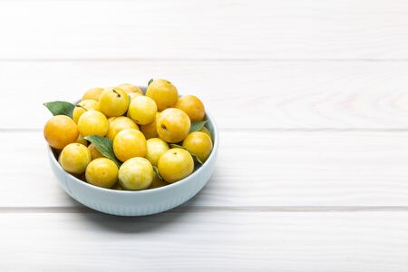 Yellow plum mirabelle fruit in bowl on white wooden table. Copy space. Healthy foodの写真素材
