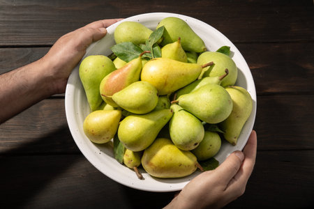 Male hands holding a bowl with organic pears on dark wooden table. Top viewの写真素材