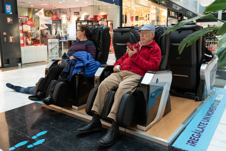 As Cancelas shopping mall, Santiago de Compostela, Spain; december 01, 2019: Senior couple sitting on massaging chair at shopping mallのeditorial素材