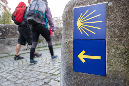 Way of St. James sign and unfocused pilgrims at background. Yellow scallop sign pilgrimage to...