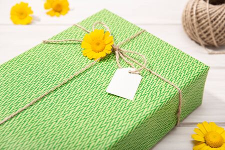 Green Gift or present box with blank label and daisy flowers on table. Mock upの写真素材
