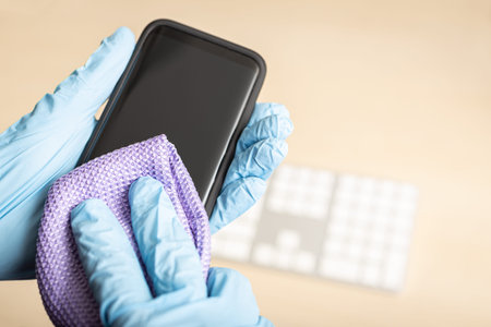 Hands with gloves cleaning mobile phone with disinfectant. COVID-19 Coronavirus outbreak...