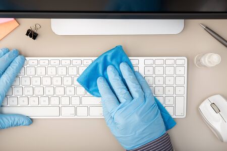Hand with protective glove cleaning a keyboard with disinfectant. COVID-19 Coronavirus outbreak prevention concept. Top viewの写真素材