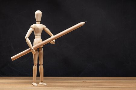 Wooden mannequin holding a pencil. Blackboard background. Drawing concept. Copy spaceの写真素材