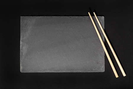 Empty Black slate Tray Plate and chopsticks on black background. Top view Mock upの写真素材