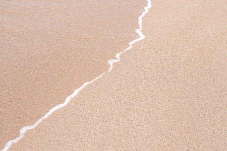 Soft beautiful sea wave on sandy beach. Background texture. Wet Sandy beach