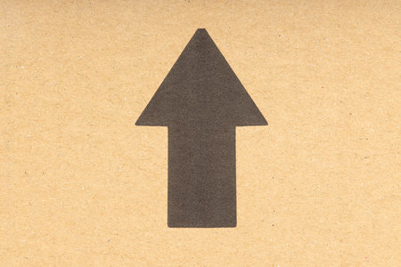 Black arrow pointing up on brown cardboard background. Close up