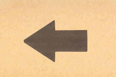 Black arrow pointing left on brown cardboard background. Close upの写真素材