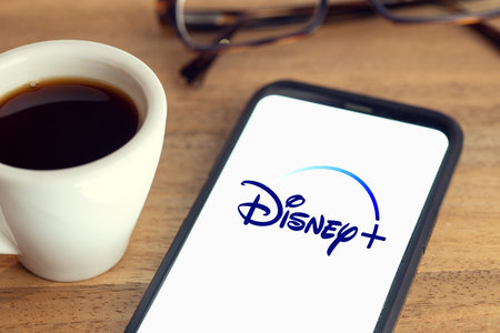 Galicia, Spain; february 15, 2021: Disney plus logo on Smart phone screen on desk with eyeglasses and cup of coffee on wooden tableのeditorial素材