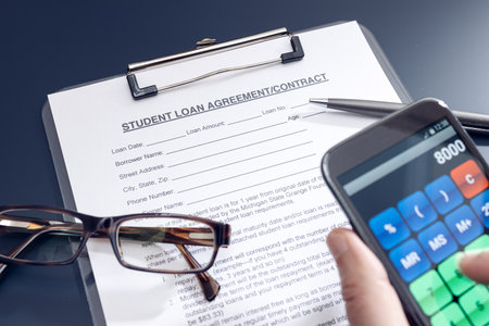 Blank Student Loan Application on table and hand holding a smartphone with calculator app. Education costの写真素材