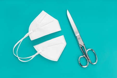 KN95 face maskcut in half and scissors isolated on blue background. Concept of no longer be required to wear face masksの写真素材