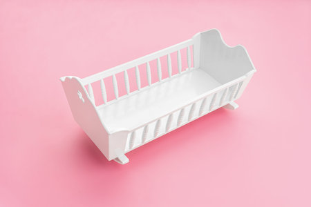 White baby crib isolated on pink background. Girl birth rate concept