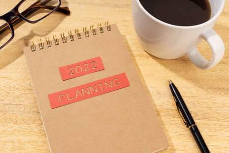 New year 2022 planning concept. Notepad, cup of coffee and eyeglasses on wooden deskの写真素材