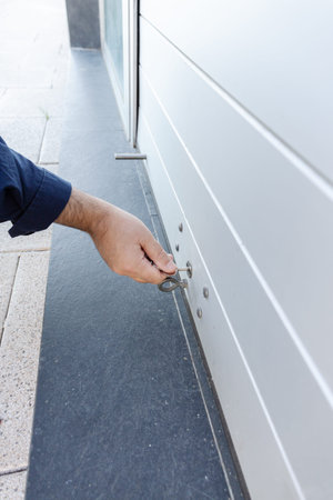 Hand with a key closing a roller shutter door of a store. Closing concept