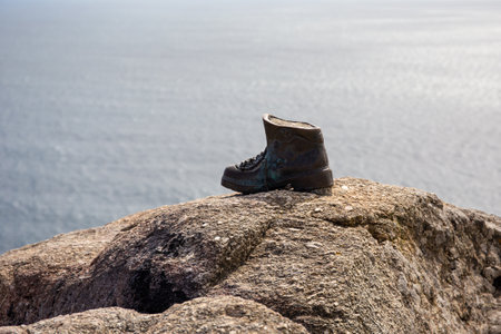 Finisterre, Spain; june 9, 2022: Cast bronze boot on the rocks at the end of Camino de Santiago. Copy spaceのeditorial素材