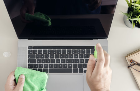 Computer cleaning concept. Top view of a male human hands cleaning a laptop screen with cleaning...